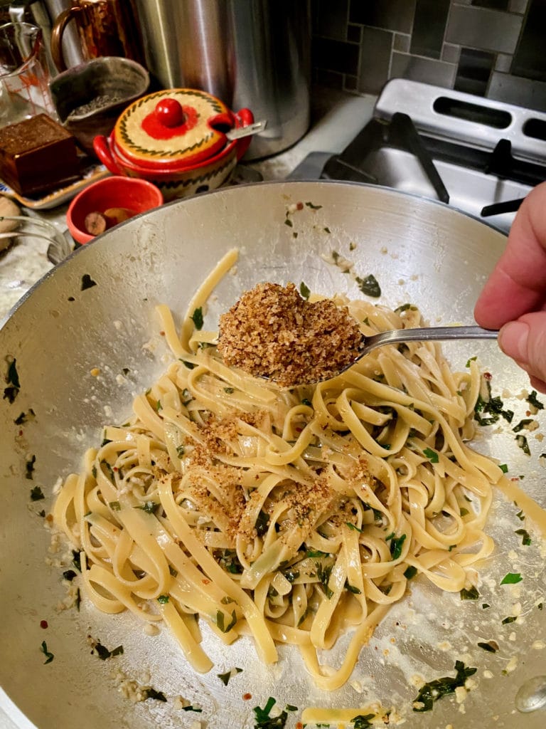 Adding breadcrumbs to cooked pasta.