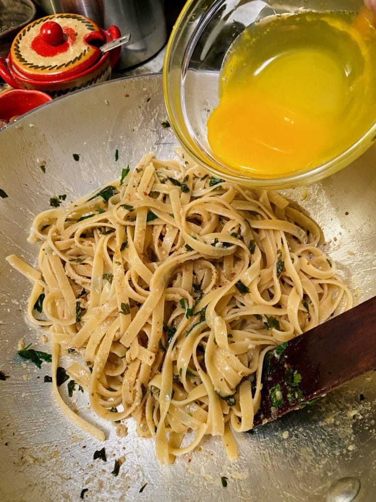 Adding egg yolks to cooked pasta.