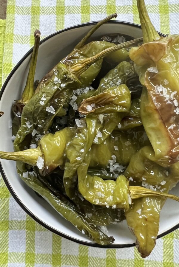 Overhead view of long hot peppers recipe in white bowl, sprinkled with coarse salt.