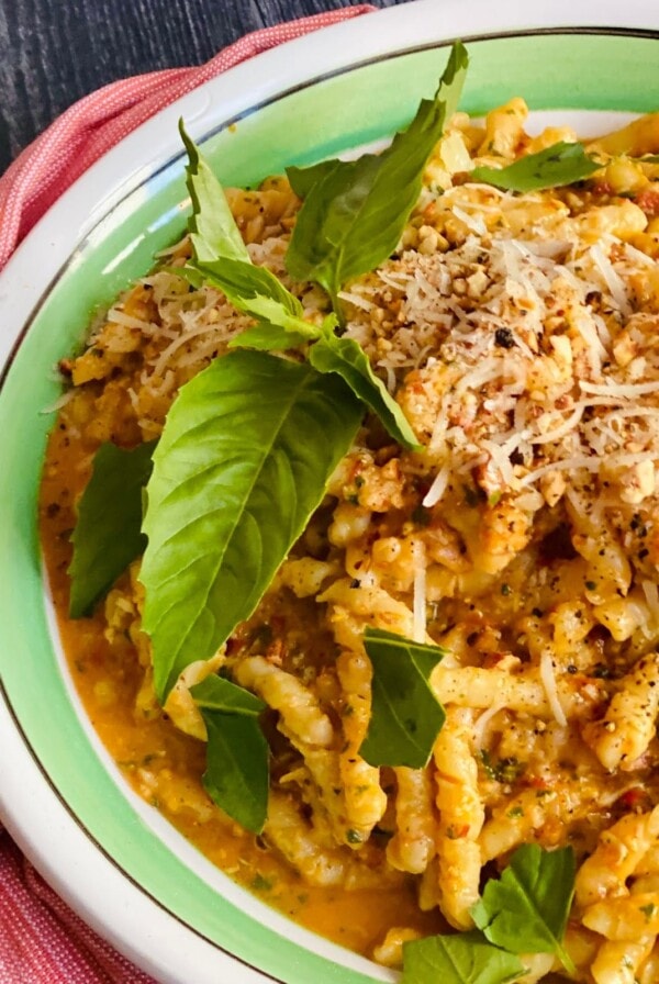 Overhead view of Pesto alla Siciliana with pasta finished in green and white bowl and garnished with fresh whole basil leaves.