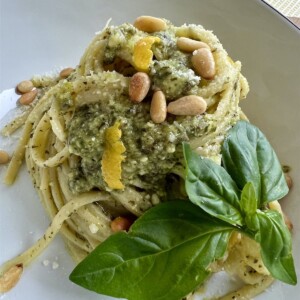 Styled portion of Pasta al Pest with lemon rind, pine nuts and basil leaves garnish.