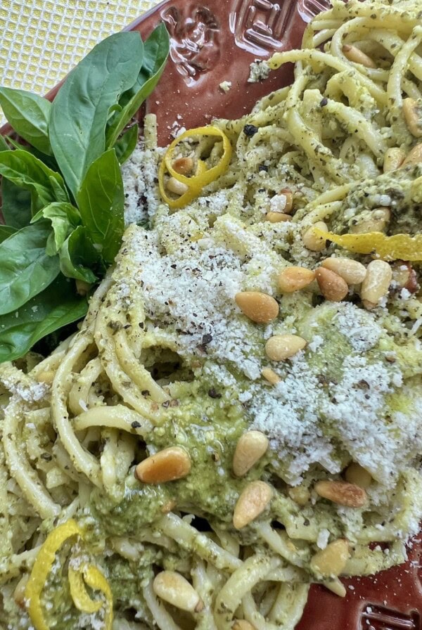 Pasta al Pesto on red platter with basil garnish, overhead view.