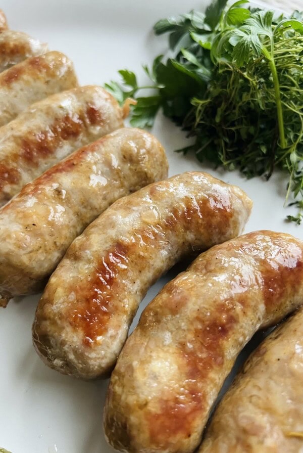 Oven baked Italian sausage on white plate with fresh herbs.