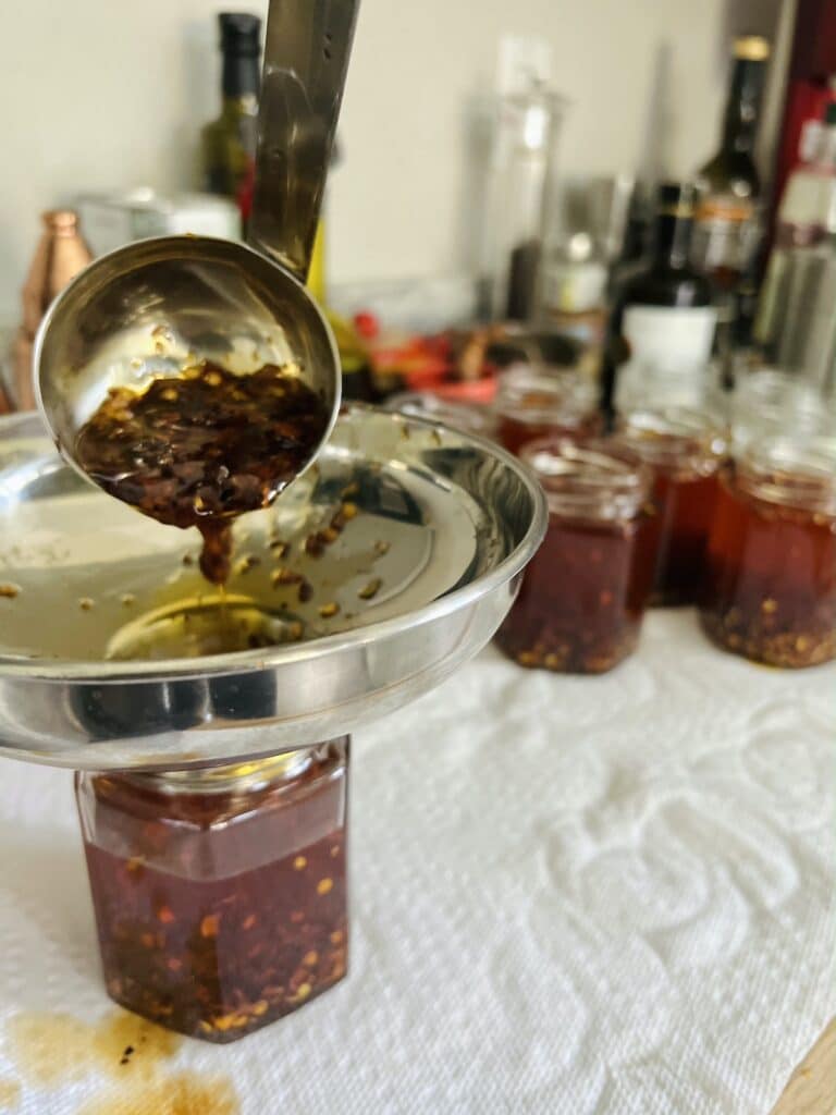 Ladle of olio di peperoncino being poured into a funnel over a glass jar.