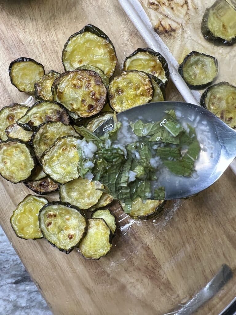 Marinated vinegar being poured over roasted sliced zucchini in bowl.