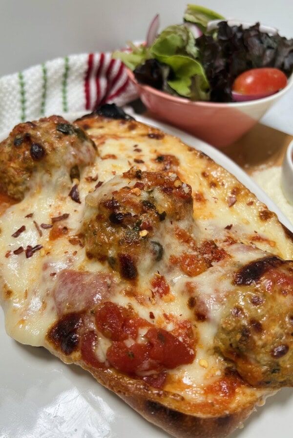 Styled photo of meatball parm hero with mixed green salad in background.