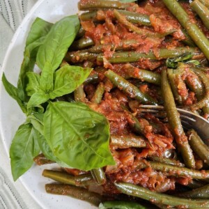 Finished Italian green beans in tomato sauce styled on plate with fresh basil garnish.