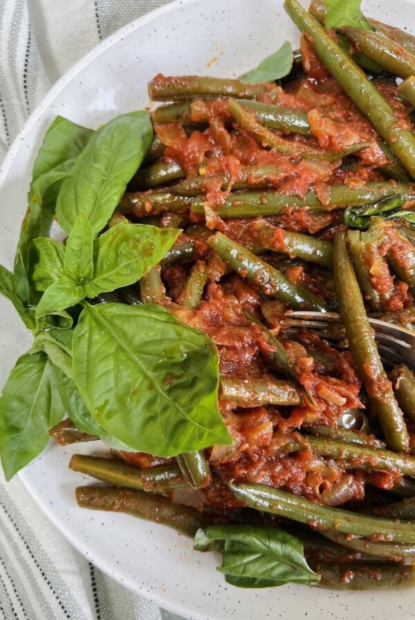Finished Italian green beans in tomato sauce styled on plate with fresh basil garnish.
