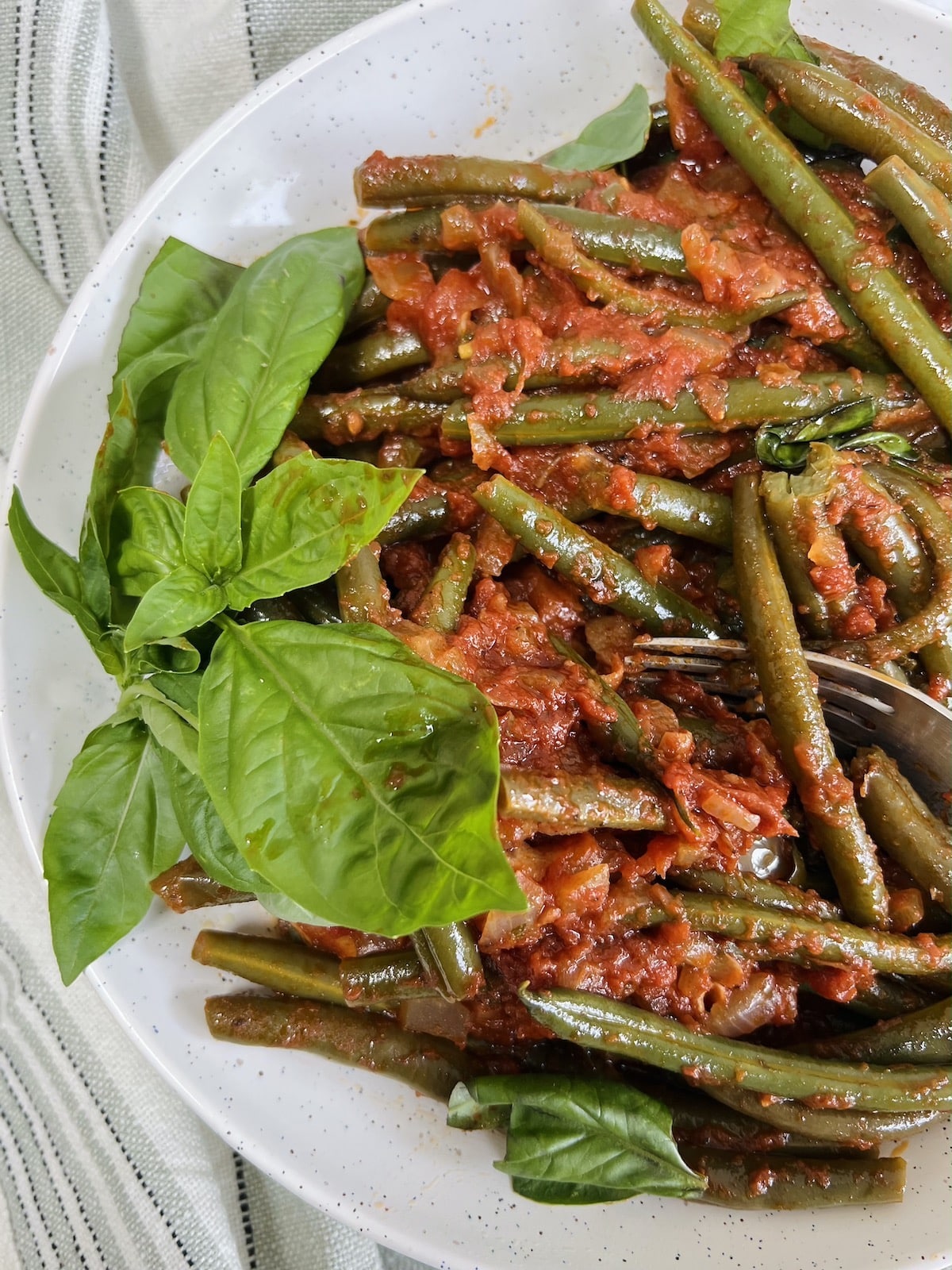 Finished Italian green beans in tomato sauce styled on plate with fresh basil garnish.