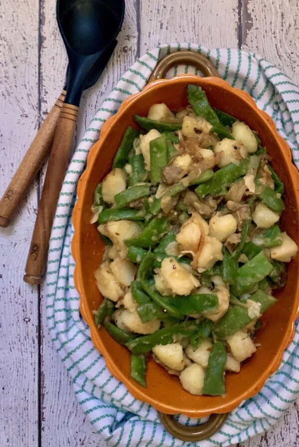 Overhead photo of italian green beans and potatoes with towel wrapped around bowl and spoon in background.