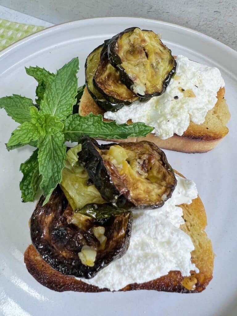 Zucchini alla scapece over ricotta on crostini with mint garnish.