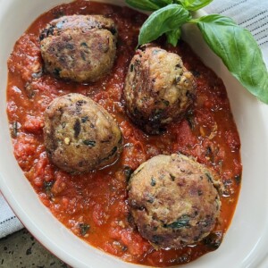 Finished polpette di melanzane without meat in tomato sauce in oval dish with basil garnish.