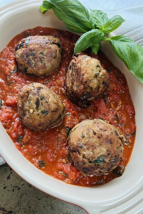 Finished polpette di melanzane without meat in tomato sauce in oval dish with basil garnish.