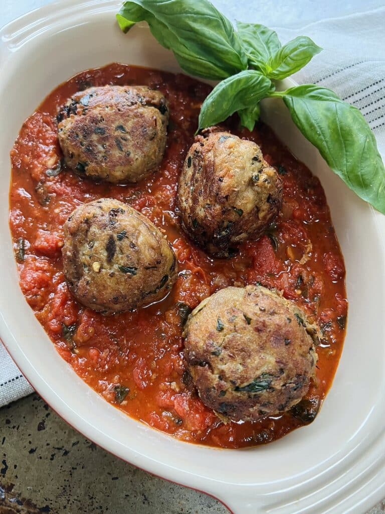 Finished polpette di melanzane without meat in tomato sauce in oval dish with basil garnish.