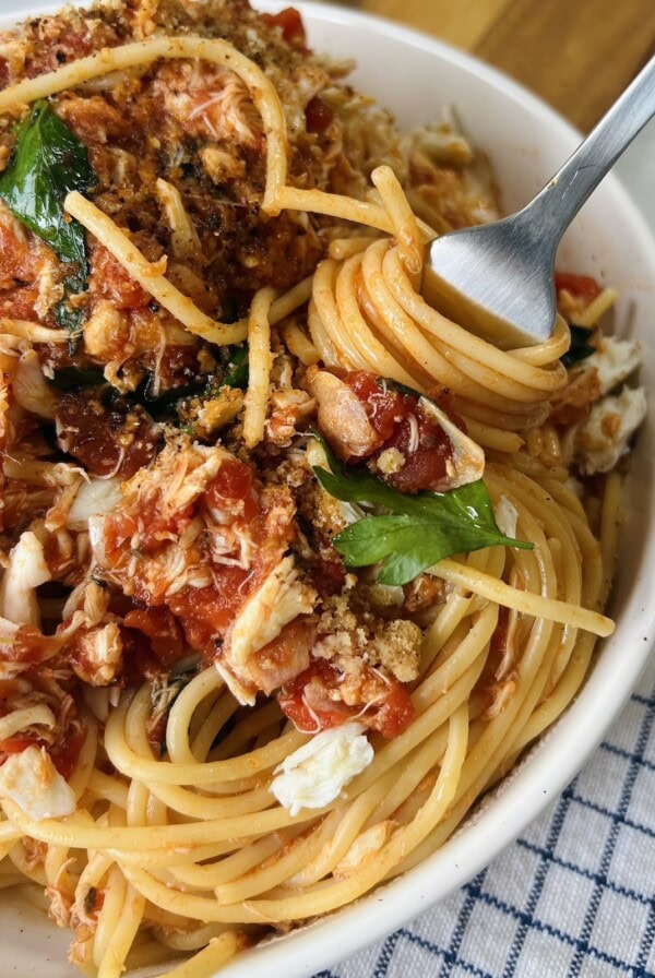 Fork twirling spaghetti in bowl of crab pasta sauce.