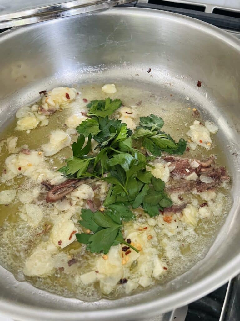 Butter, oil, garlic, anchovy, crushed red pepper and parsley being cooked in pan.