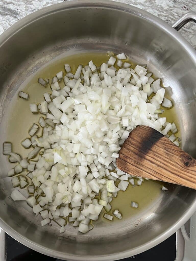 Diced onions in olive oil in pan with wooden spoon.