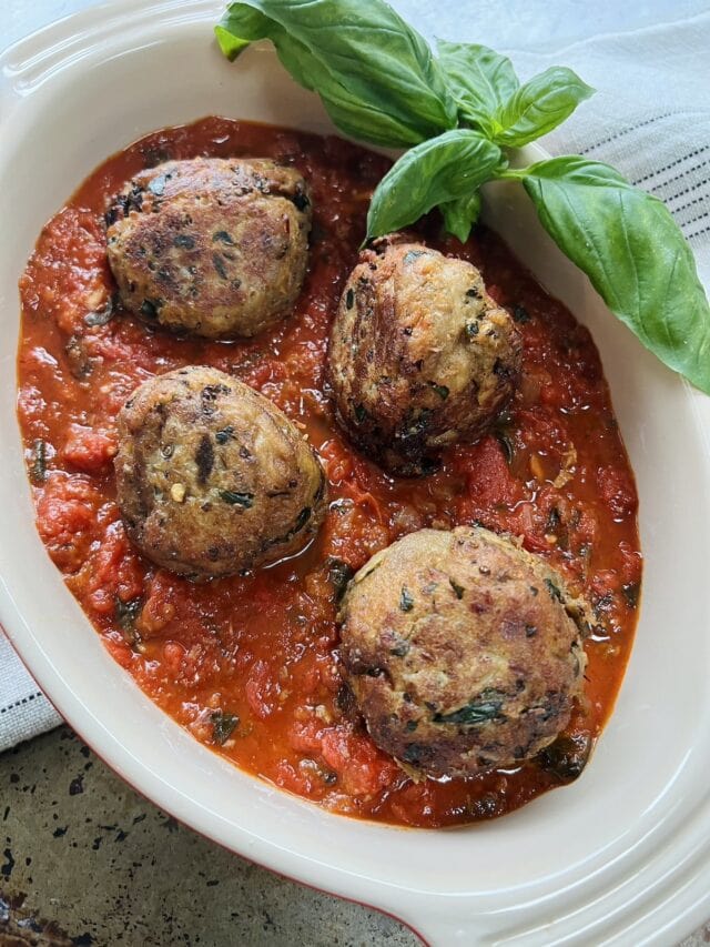 Finished polpette di melanzane without meat in tomato sauce in oval dish with basil garnish.