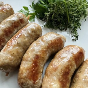 Oven Baked Italian sausage on white plate with fresh herbs.