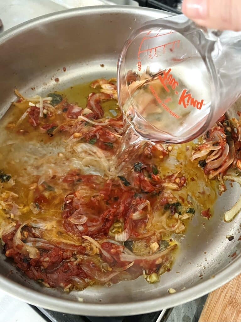 Vodka being added to pan with onion mixture.
