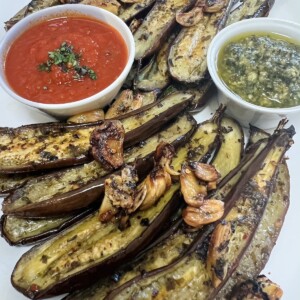 Roasted baby eggplant styled on white platter with crispy garlic, pesto and tomato sauce.