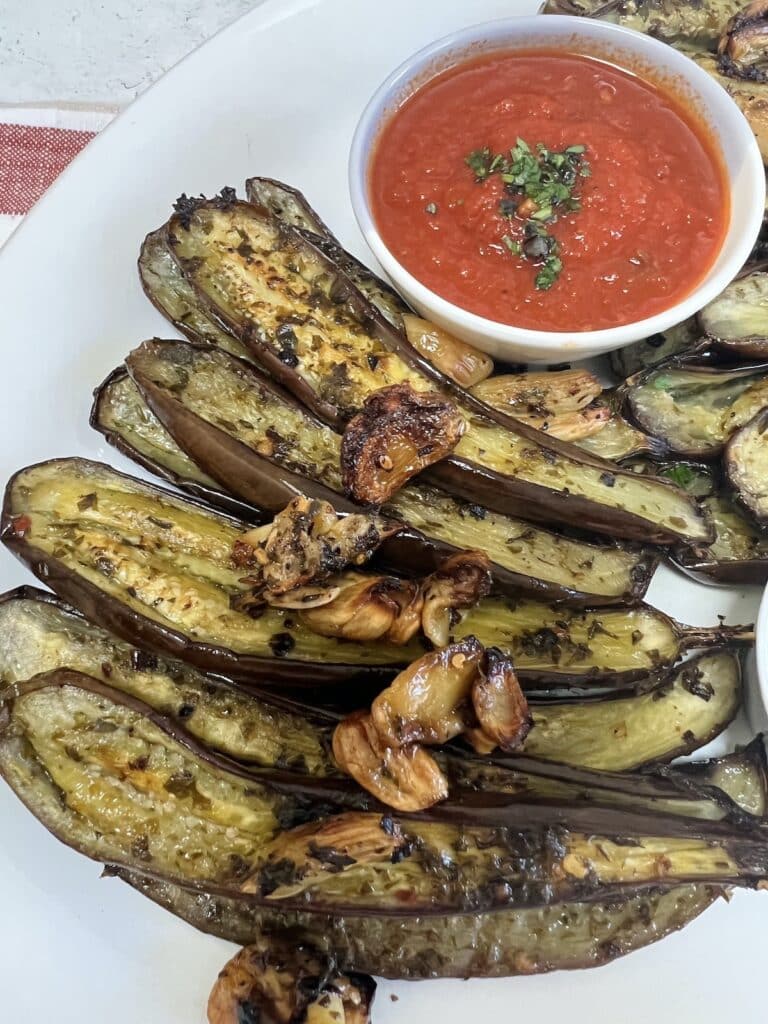 Roasted baby eggplant styled on white platter with crispy garlic and tomato sauce.