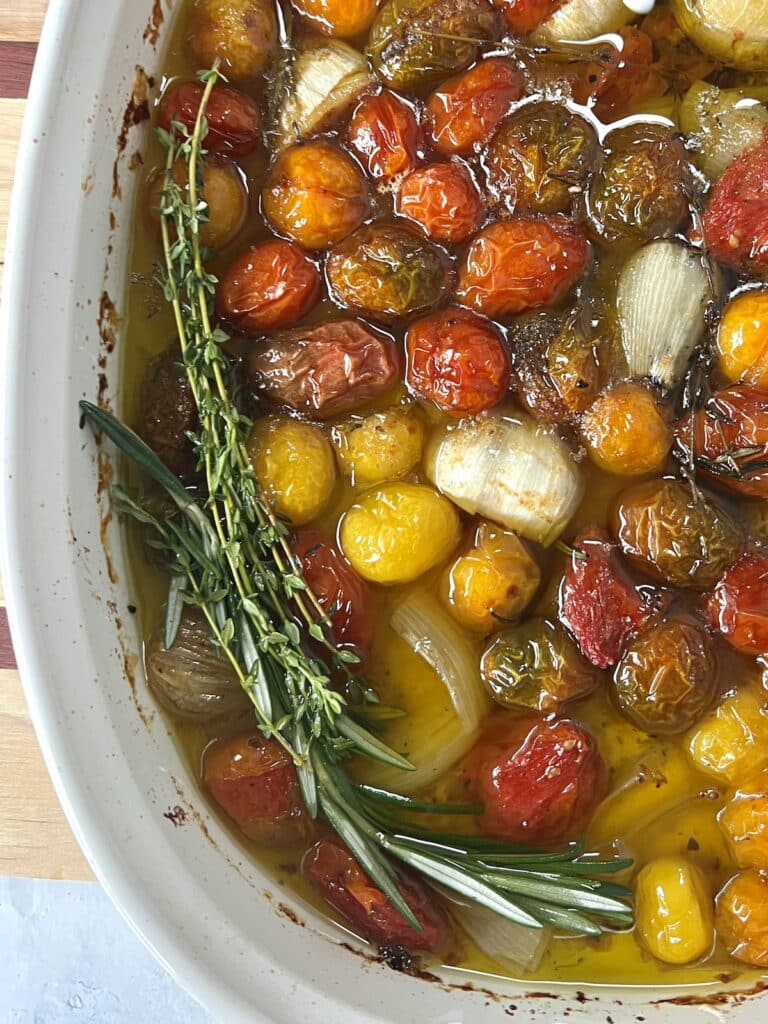 Close up of corner of finished Confit Cherry Tomatoes and Garlic in curved, rectangular baking pan.