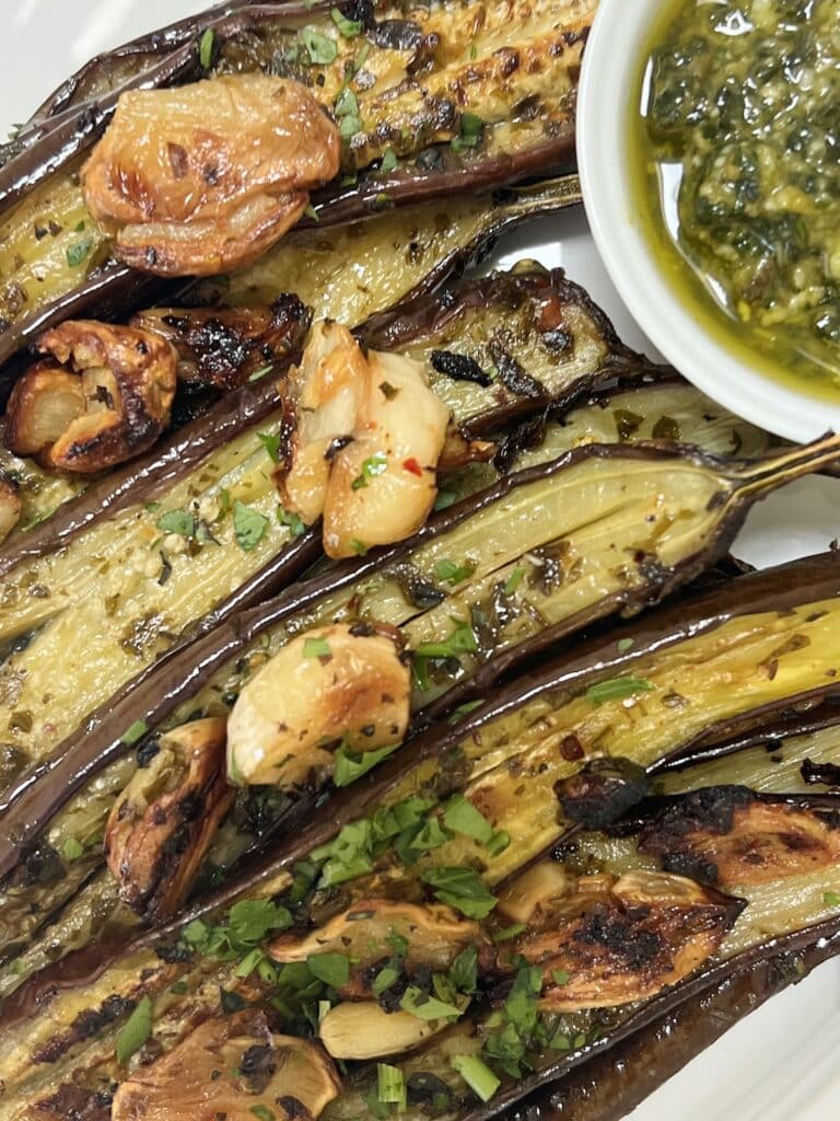 Close-up of Roasted baby eggplant styled on white platter with crispy garlic and pesto.