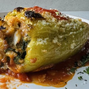 Close up of Sausage stuffed cubanelle pepper on white plate with parsley garnish.
