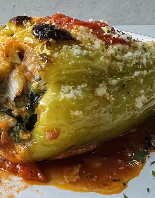 Close up of Sausage stuffed cubanelle pepper on white plate with parsley garnish.
