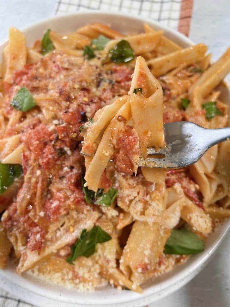 Overhead view of pasta on fork over bowl of Homemade vodka sauce with fresh tomatoes.