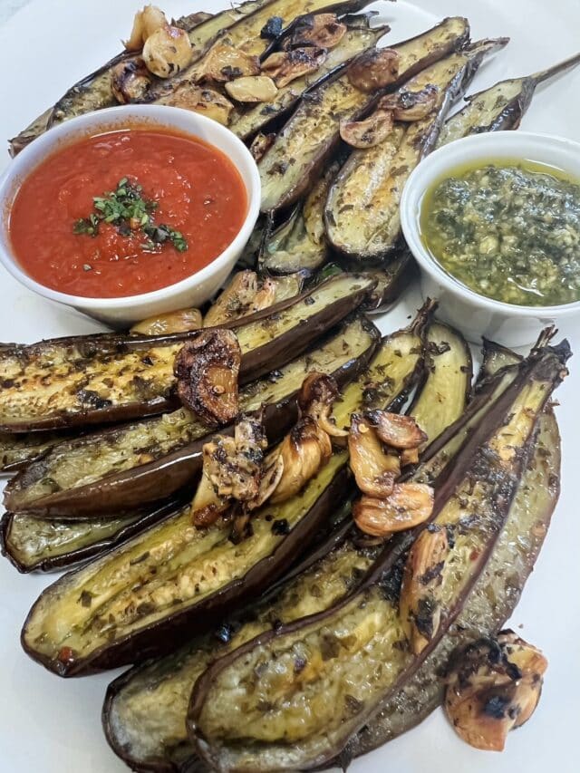 Roasted baby eggplant styled on white platter with crispy garlic, pesto and tomato sauce.