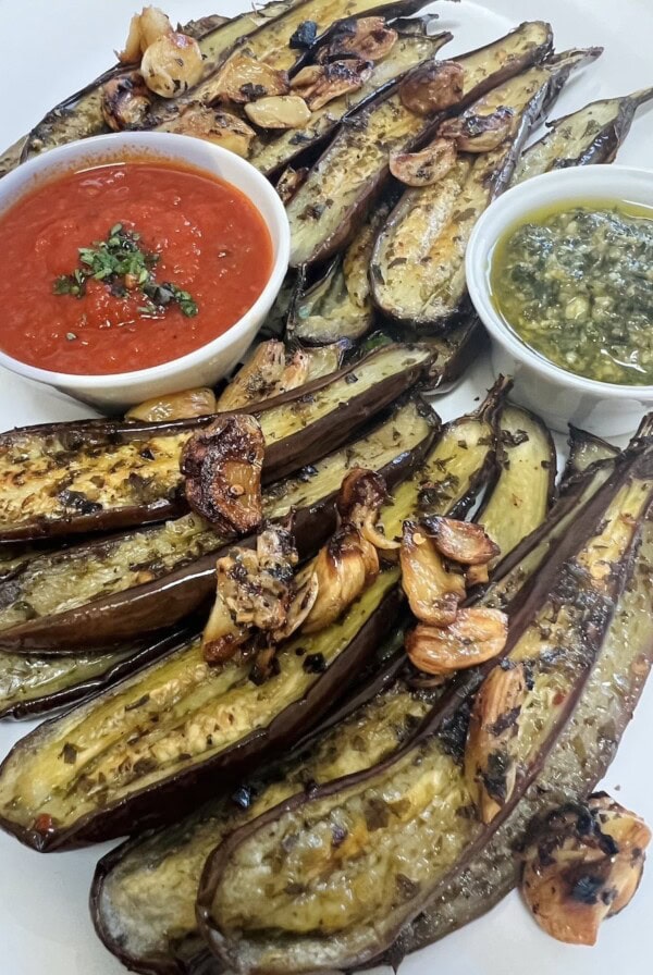 Roasted baby eggplant styled on white platter with crispy garlic, pesto and tomato sauce.