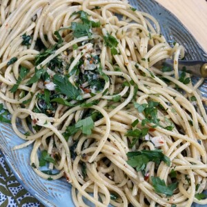 Finished Spaghetti aglio olio peperoncino on blue platter.