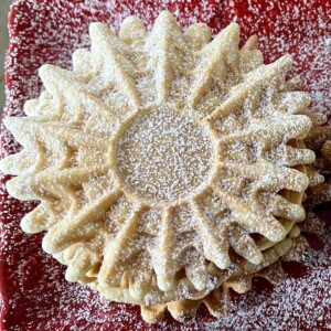Anise pizzelle dusted with powdered sugar on red plate.