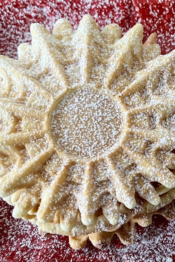 Anise pizzelle dusted with powdered sugar on red plate.