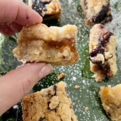 Close up of piece of Layered Cookie Bars with Nuts and Jam on green dish with powdered sugar.