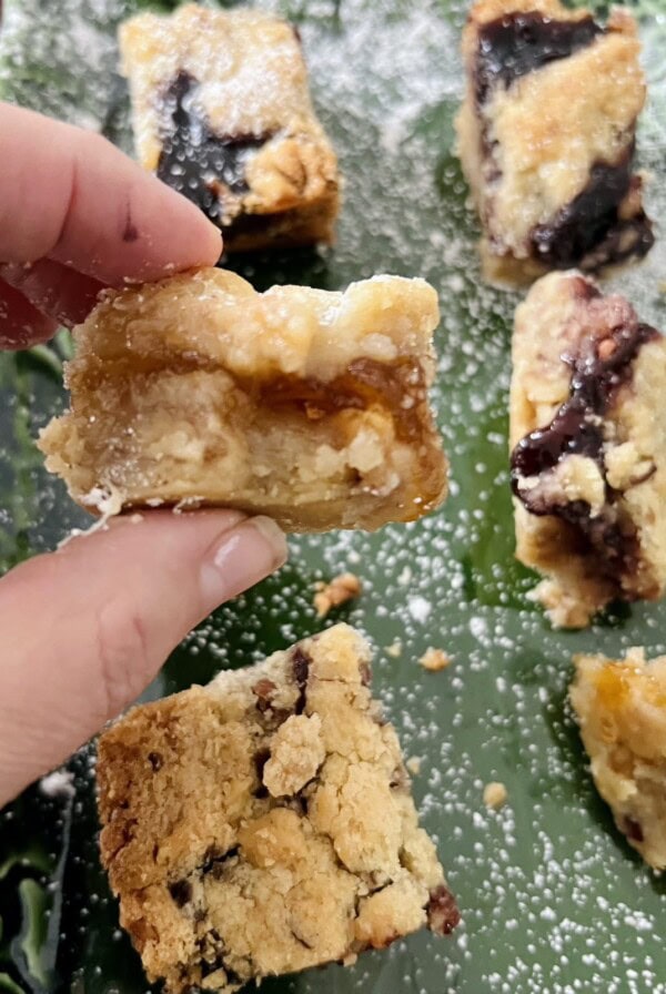 Close up of piece of Layered Cookie Bars with Nuts and Jam on green dish with powdered sugar.