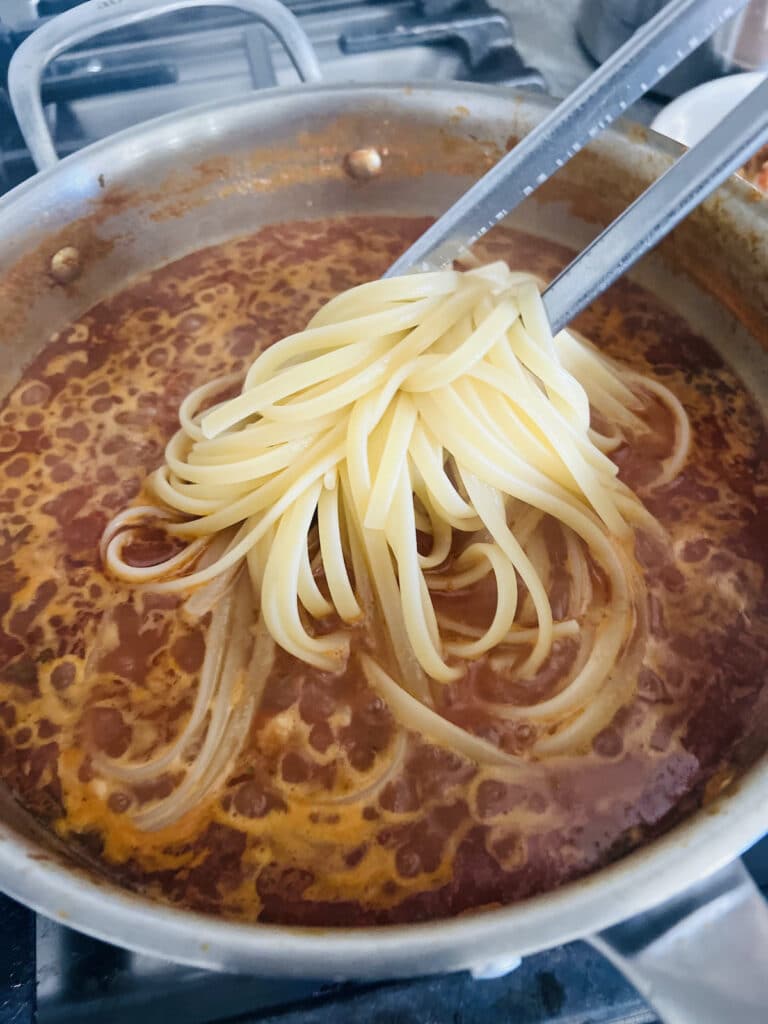 Adding cooked linguine to tomato clam sauce.