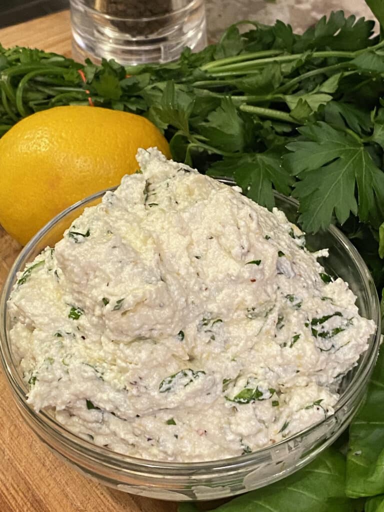Finished herb ricotta with lemons and herbs in background.