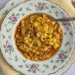 Pasta e patate in decorative soup bowl with spoon on yellow towel.