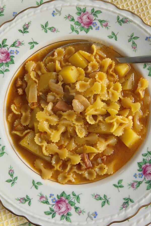 Pasta e patate in decorative soup bowl with spoon on yellow towel.