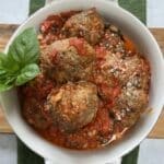 Fried meatballs in marinara sauce in white bowl with basil garnish.