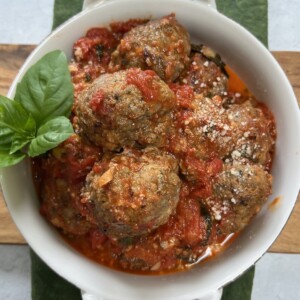 Fried meatballs in marinara sauce in white bowl with basil garnish.