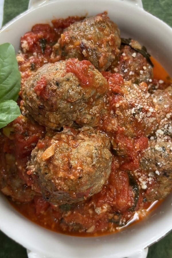 Fried meatballs in marinara sauce in white bowl with basil garnish.