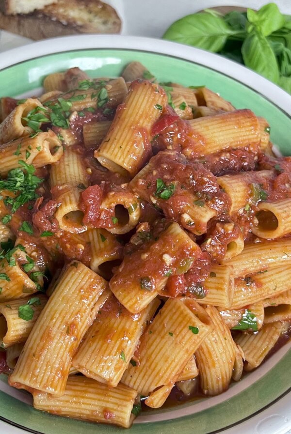 Rigatoni Arrabbiata in pasta bowl with italian bread and basil in background.