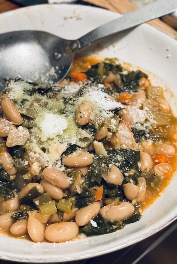 Escarole and White Bean Soup in white bowl with large spoon.