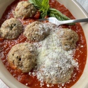 Meatballs no bread crumbs in tomato sauce with basil garnish, grated cheese and fork in baking dish.