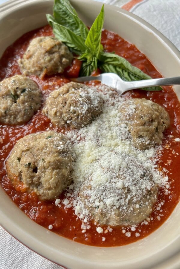 Meatballs no bread crumbs in tomato sauce with basil garnish, grated cheese and fork in baking dish.