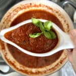 Finished sauce from frozen tomatoes in gravy boat with basil garnish over pot of sugo in background.